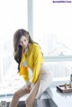 A woman in a yellow shirt and white skirt sitting on a counter.