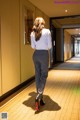 A woman in a white shirt and gray pants walking down a hallway.