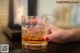 A person holding a glass of whiskey on a counter.