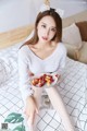 A woman sitting on a bed holding a plate of fruit.