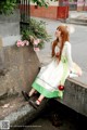 A woman in a white and green dress sitting on a stone wall.