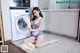 A woman sitting on the floor in front of a washing machine.