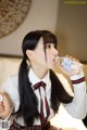 A woman in a school uniform drinking water from a bottle.