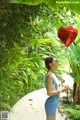 A woman holding a red heart shaped balloon in a park.