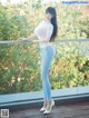 A woman in a white top and blue jeans posing on a balcony.