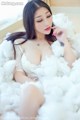 A woman in a white dress sitting on a bed covered in fluffy white clouds.