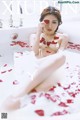 A woman sitting in a bathtub with rose petals on the floor.