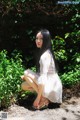 A woman in a white dress crouching down in the woods.