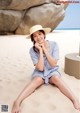 A woman sitting on the beach wearing a straw hat.