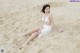 A woman in a white bikini sitting on the sand.