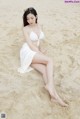 A woman in a white bikini sitting on the sand.