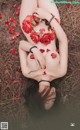 A woman laying on the ground covered in red roses.