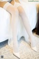 A woman wearing white stockings and high heels sitting on a bed.