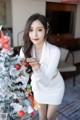 A woman in a white dress standing next to a Christmas tree.