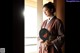 A woman in a kimono holding a fan in front of a window.