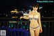 A woman in a bikini standing on a balcony at night.