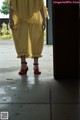 A woman in a yellow dress and red shoes standing in front of a door.