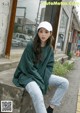 a woman sitting on a ledge wearing a green sweatshirt and jeans