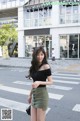 A woman in a black top and green skirt crossing the street.