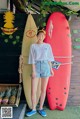 A woman standing next to a red surfboard in front of a wall.