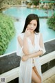 A woman in a white dress posing by a pool.