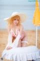 A woman in a bikini and hat sitting on a beach.