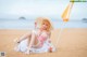 A woman in a pink bathing suit and hat sitting on a beach.