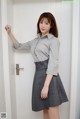 a woman in a gray shirt and skirt leaning against a door