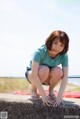 A woman crouching down on a concrete wall by the water.