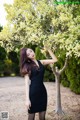 A woman in a black dress standing next to a tree.