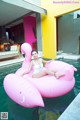 A woman in a white bathing suit sitting on an inflatable flamingo.