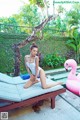 A woman in a white bathing suit sitting on a lounge chair next to a pool.